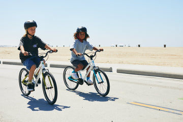 Two children riding Biky kids bikes on a paved beach path
