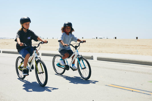 Two children riding Biky kids bikes on a paved beach path