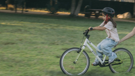 Young child wearing a helmet riding a Biky Air 14 bike with support from a parent